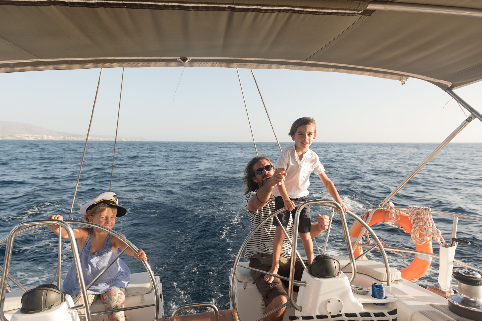 People sailing on a boat with ocean waves and orange life rings under a canopy