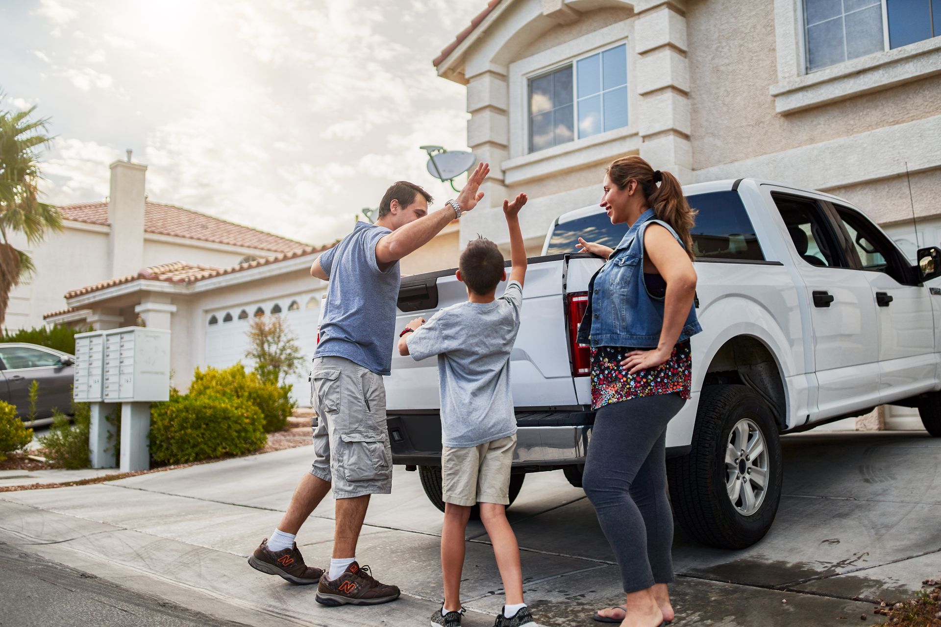 Family holding a small object in front of a white pickup truck outside a suburban house