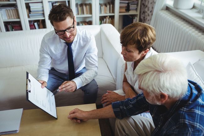 Three people in an office review a chart on a laptop while seated together on a couch.
