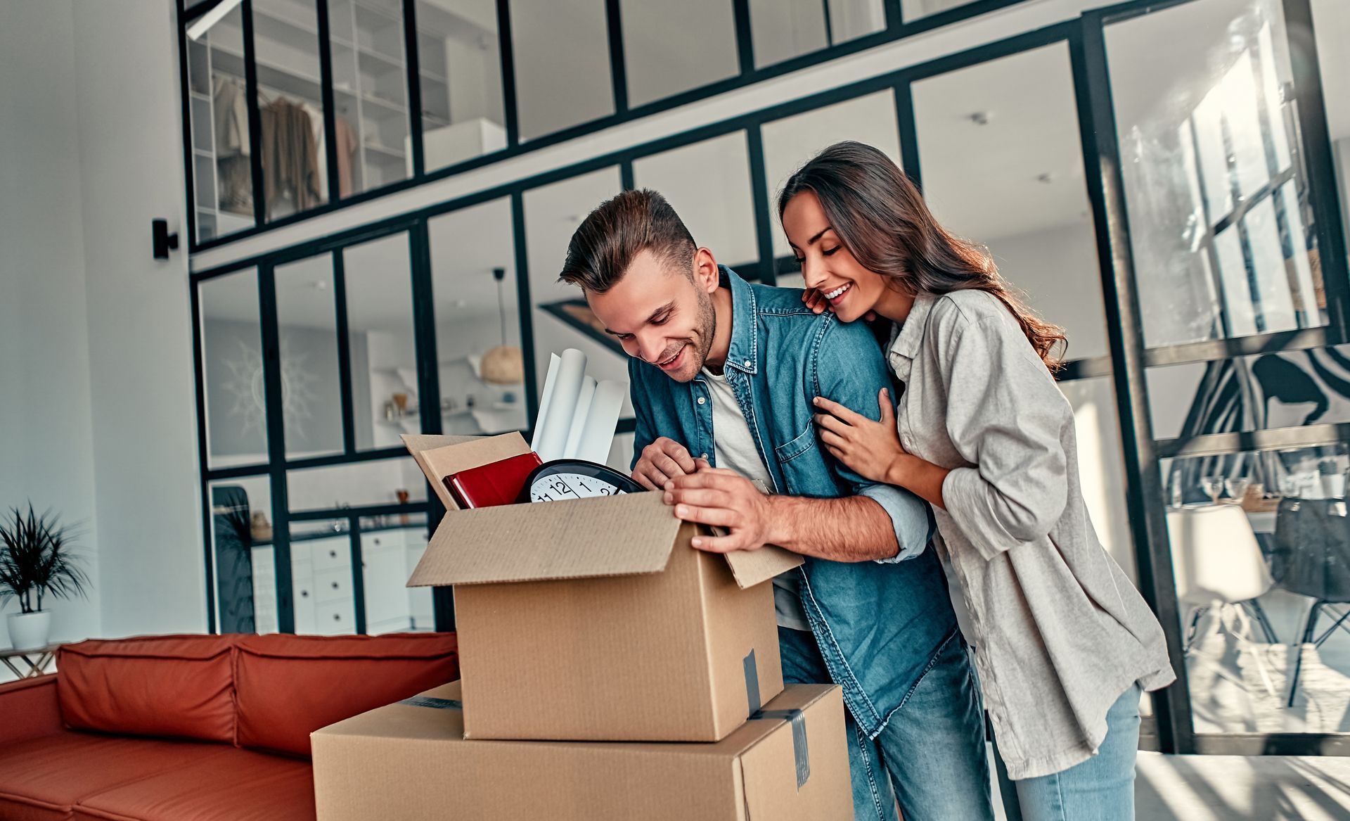 Couple unpacking boxes in a bright modern apartment, smiling together near a couch