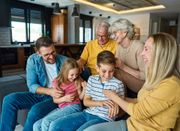 Family sitting together on a couch, smiling and using a tablet in a cozy living room.