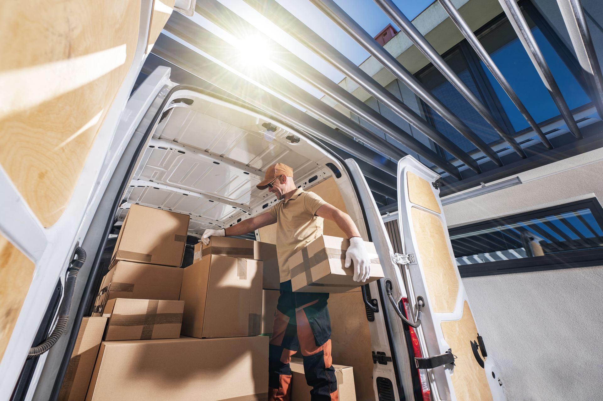 Worker stacking cardboard boxes inside a delivery van under bright daylight