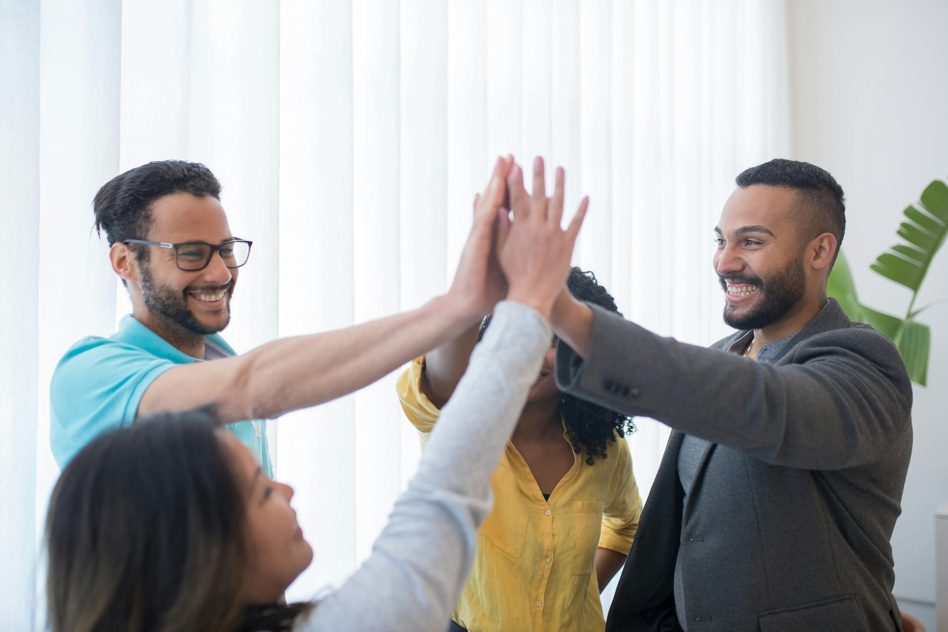 Four coworkers high-five in an office, smiling and celebrating together.
