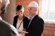 Two people in a construction site review plans, one wearing a hard hat and smiling.