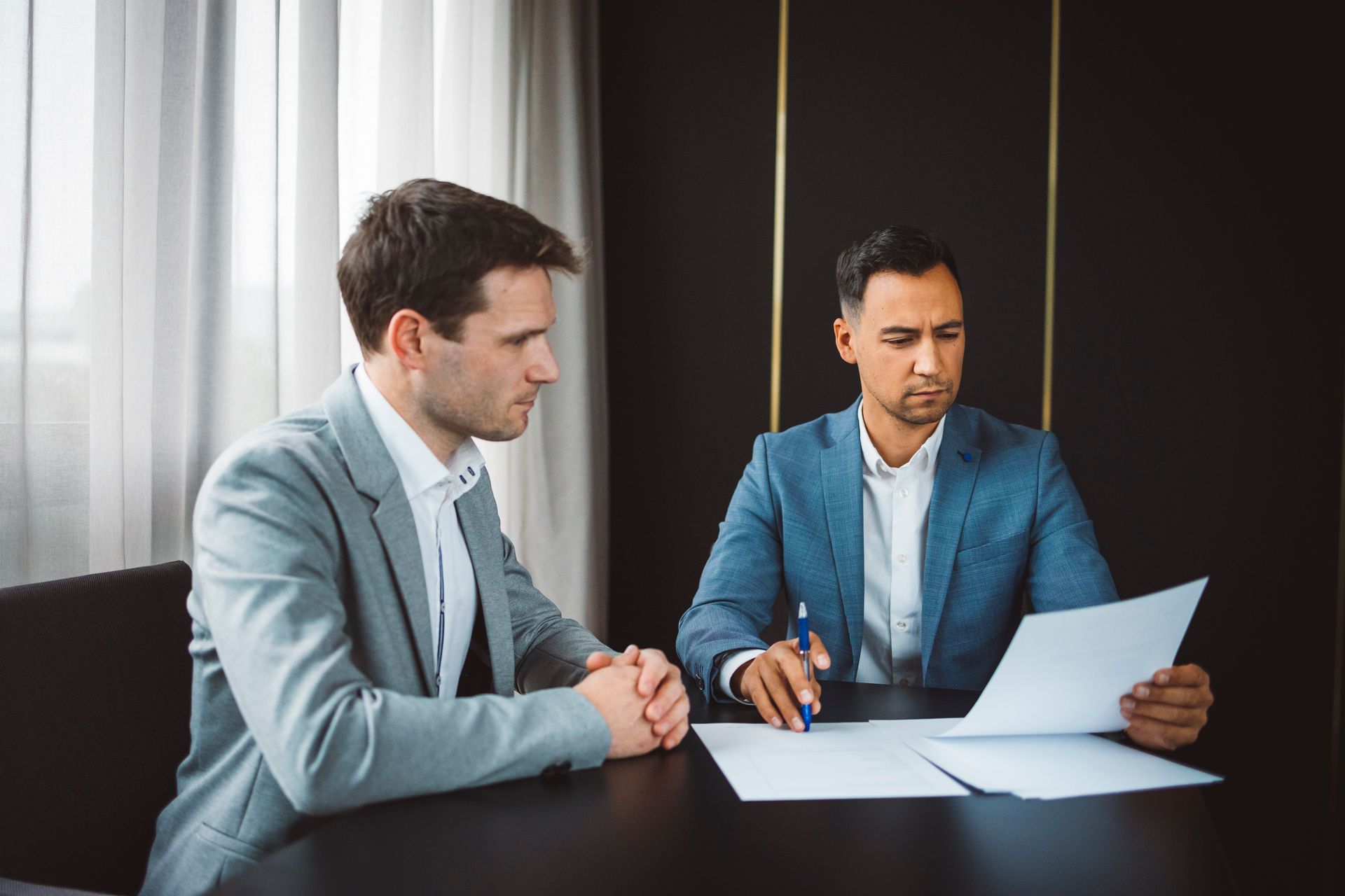 Two people in blue blazers reviewing a document at a table in a meeting room.