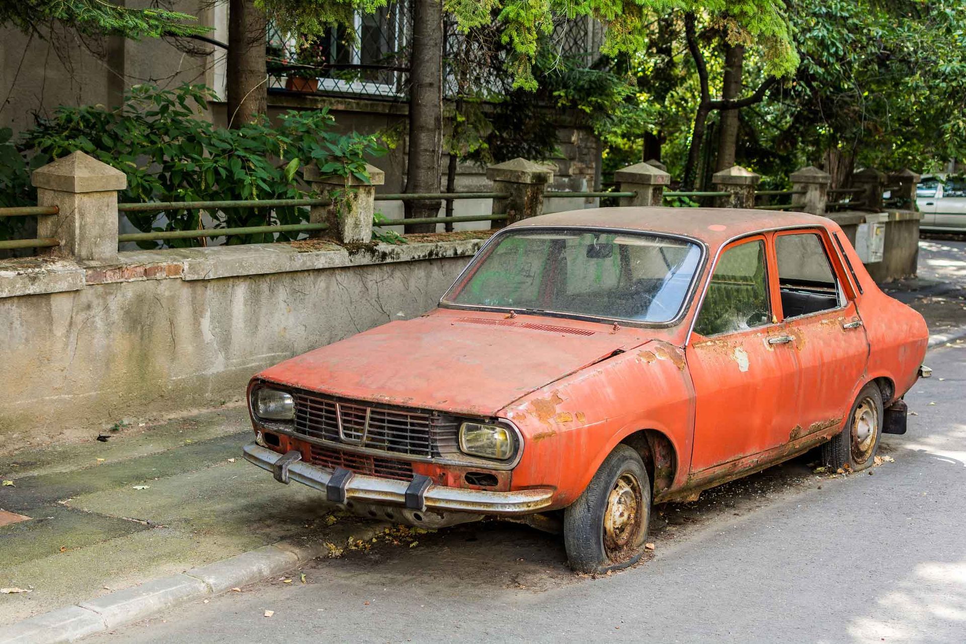 An old rusty red car is parked on the side of the road. An old rusty red car is parked on the side of the road.