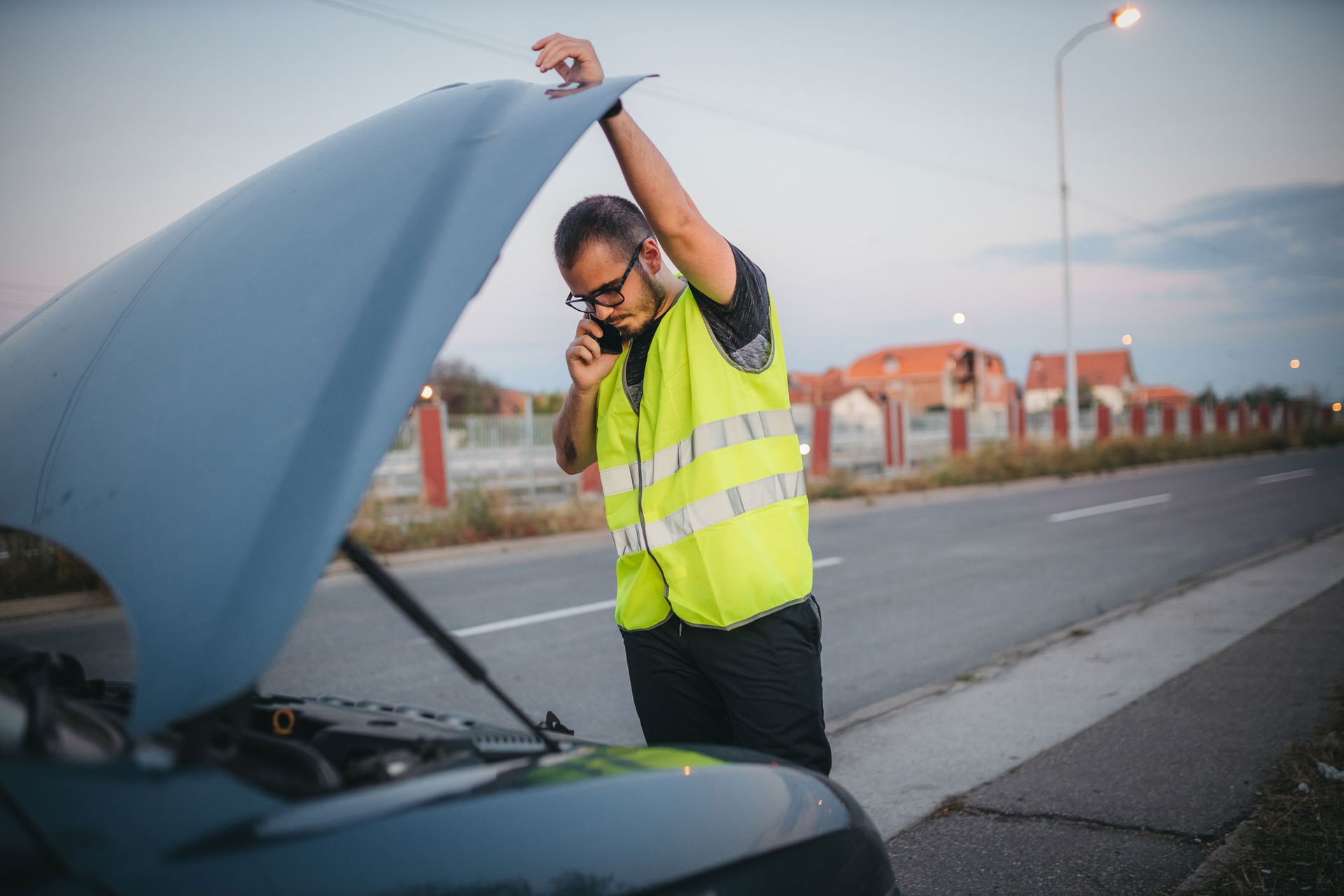 A man is standing next to a broken down car with the hood open and talking on a cell phone. A man is standing next to a broken down car with the hood open and talking on a cell phone.