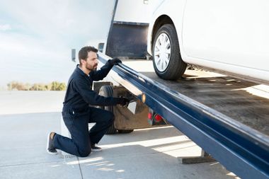 A man is kneeling down next to a tow truck. A man is kneeling down next to a tow truck.