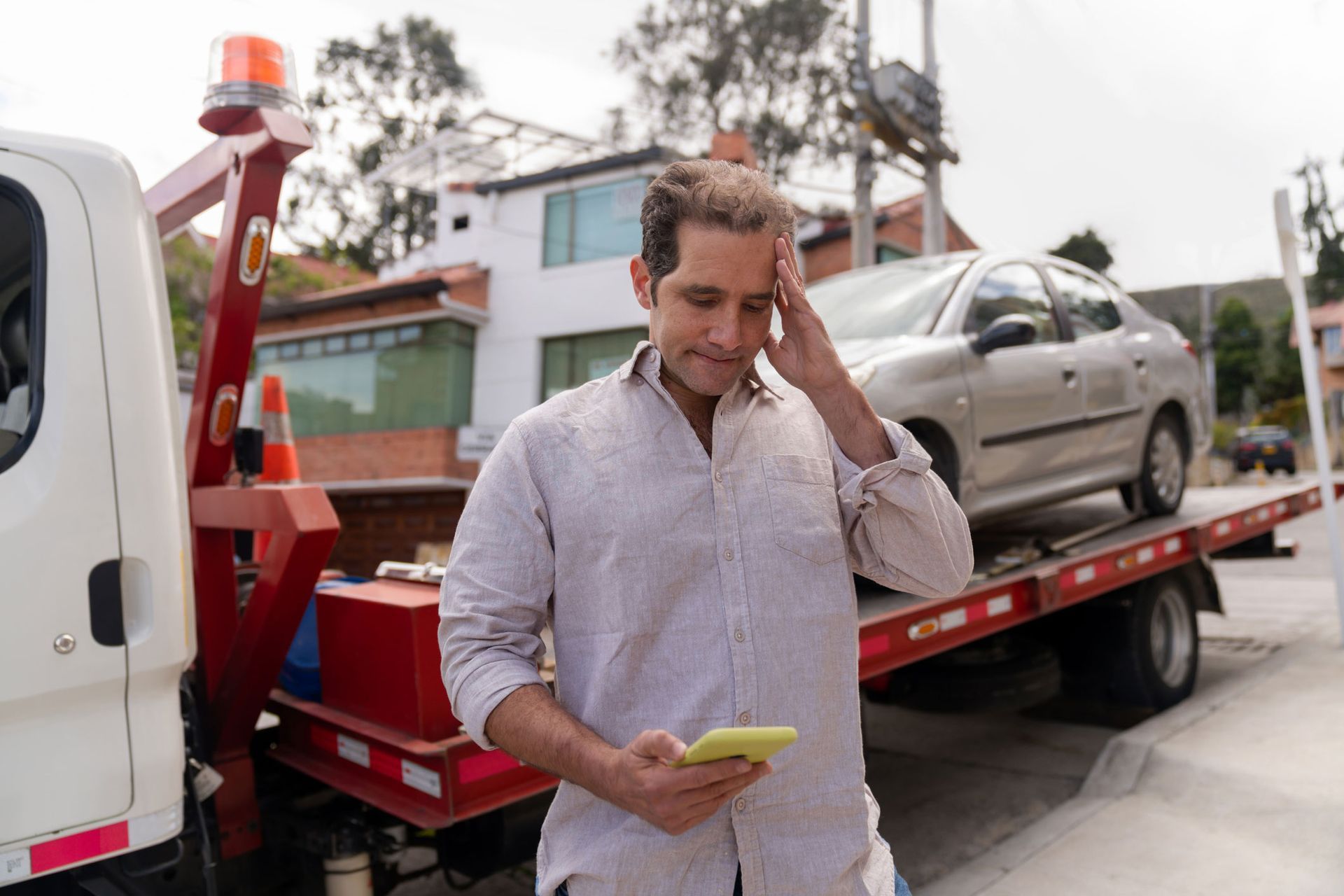 A man is standing in front of a tow truck looking at his cell phone.