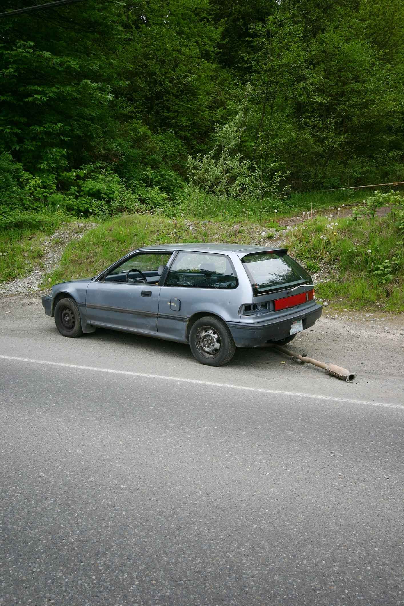 A car is parked on the side of the road next to a forest. A car is parked on the side of the road next to a forest.