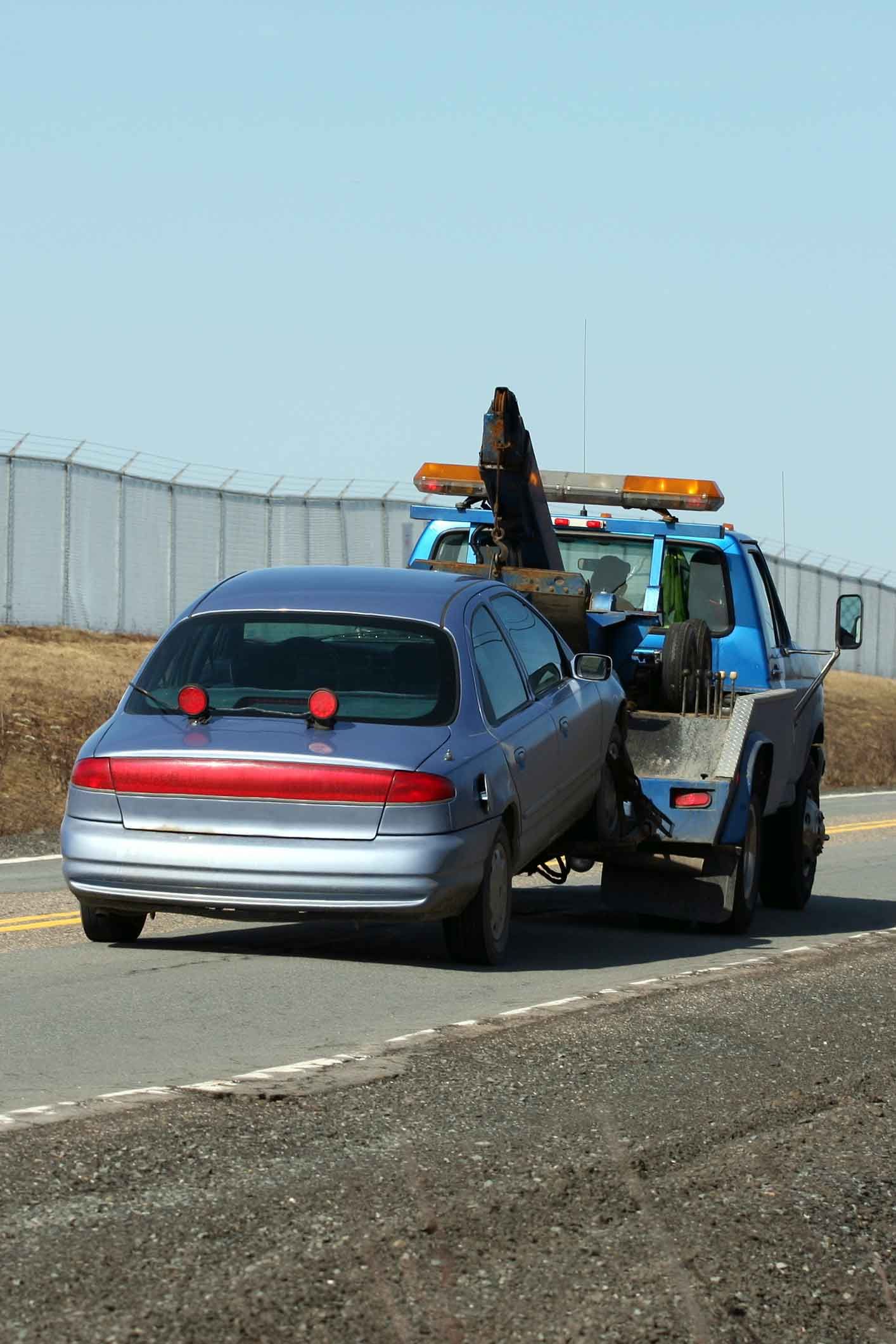 A car is being towed by a tow truck on the side of the road. A car is being towed by a tow truck on the side of the road.