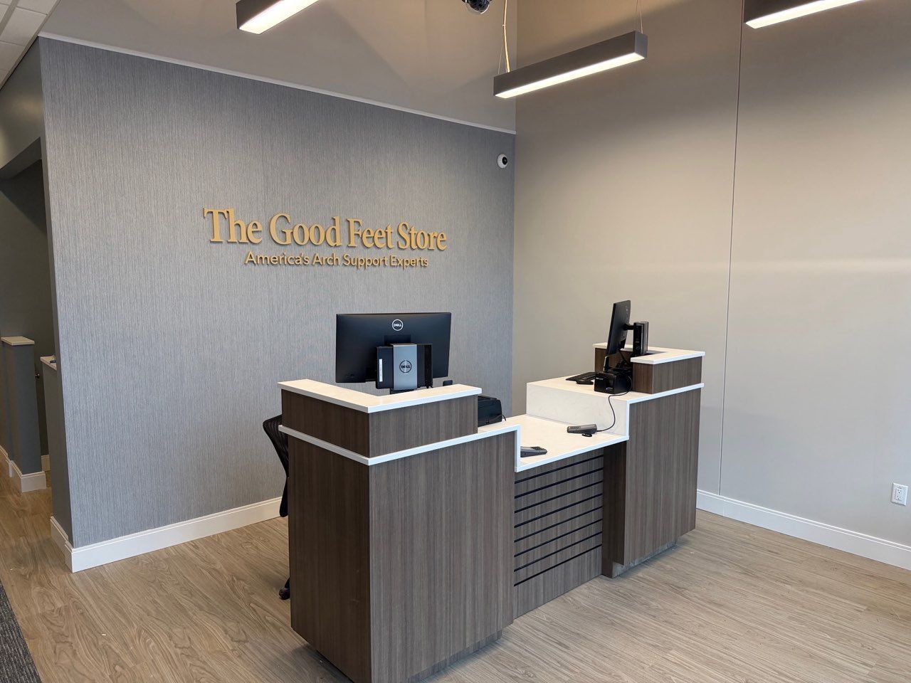 Reception desk with wood paneling and computers in front of a gray wall with The Good Feet Store logo in gold lettering.