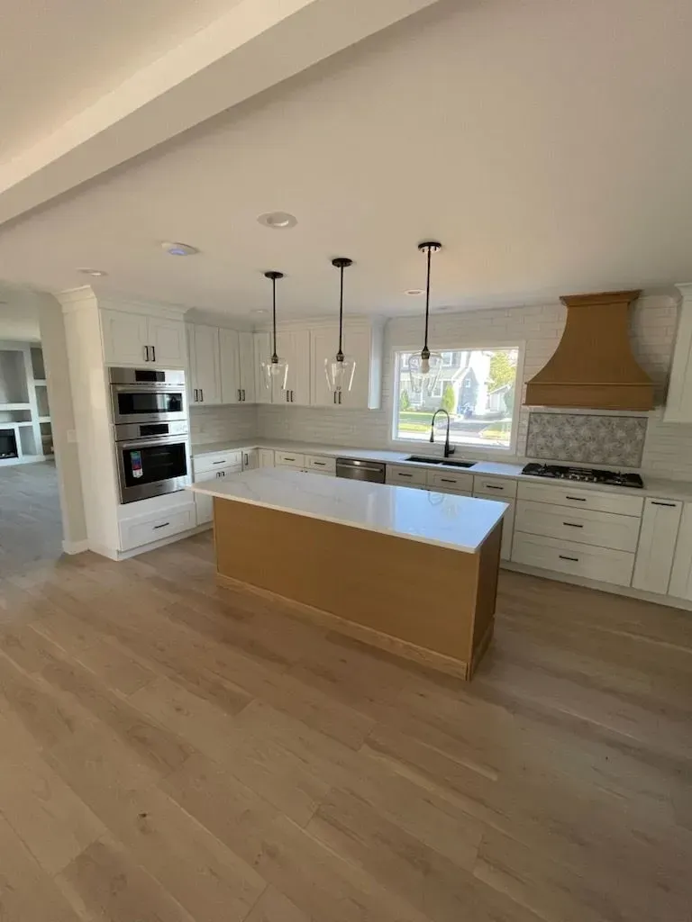 A modern kitchen featuring white cabinets, a light wood kitchen island with a white top, stainless appliances, and pendants.
