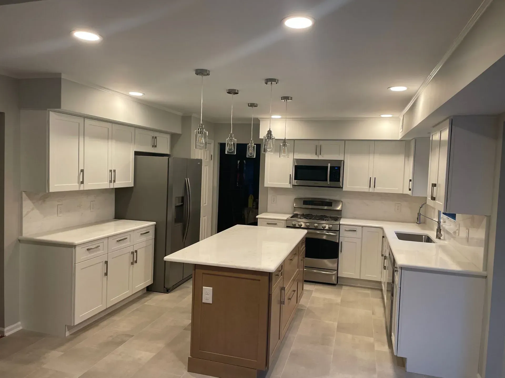 Modern kitchen with white cabinets, light countertops, stainless steel appliances, and a central island with pendant lights.
