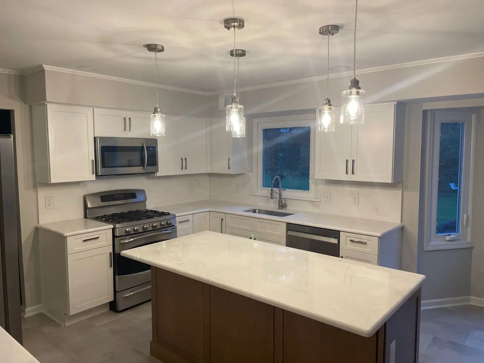 A modern kitchen with white cabinets, light countertops, a wooden island, stainless steel appliances, and pendant lights.