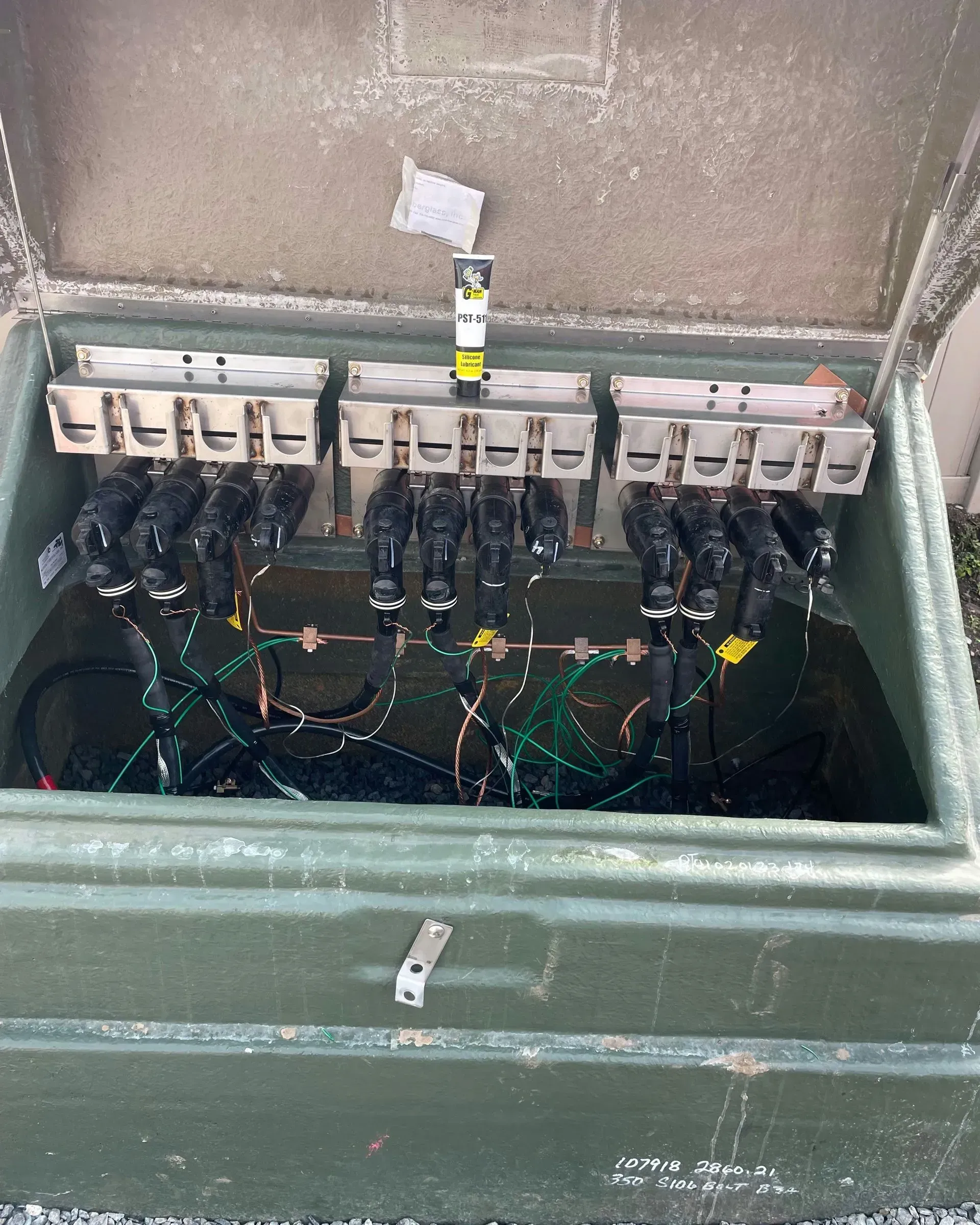 An open green electrical utility box containing multiple cables connected to three metal bus bar blocks.