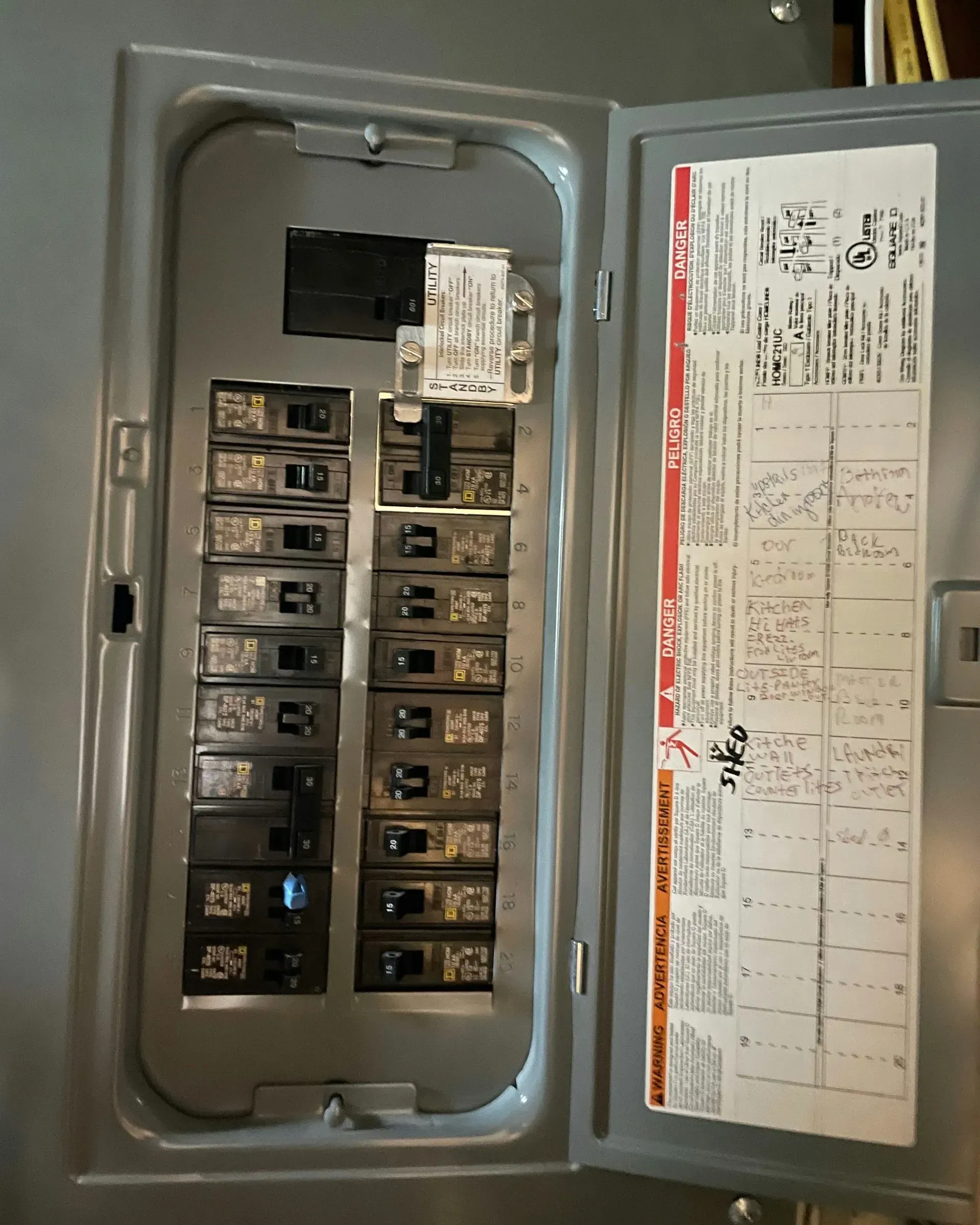 An open electrical breaker panel with multiple switches, some marked with handwritten labels on the interior door.