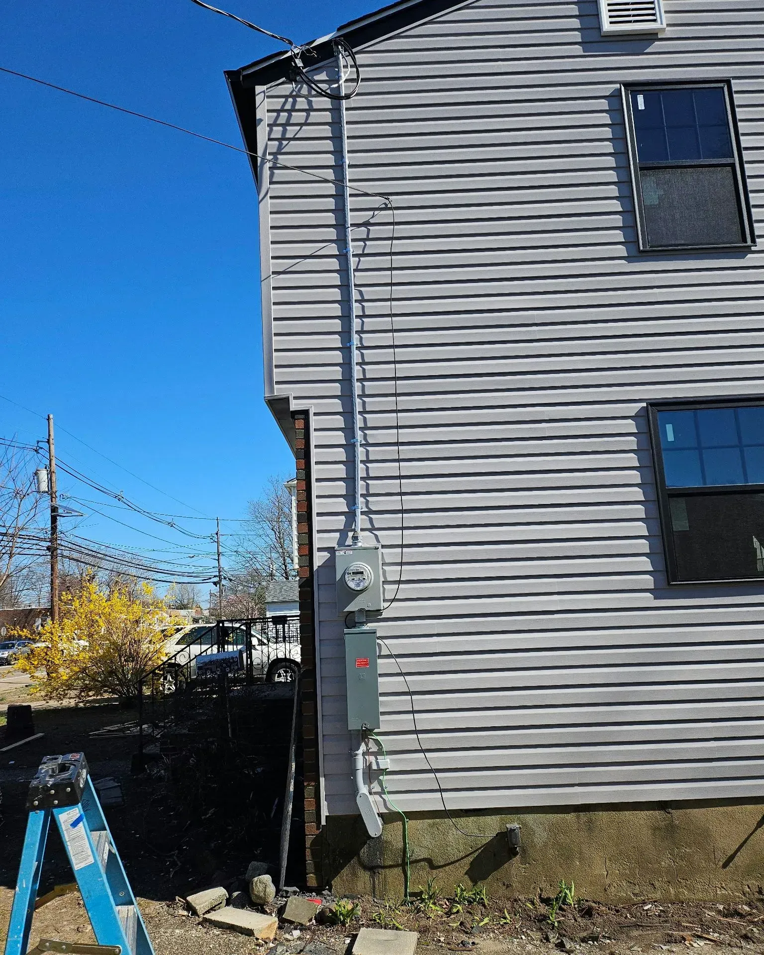 An exterior view of a grey-sided house showing a newly installed electrical meter and service panel on the corner wall.