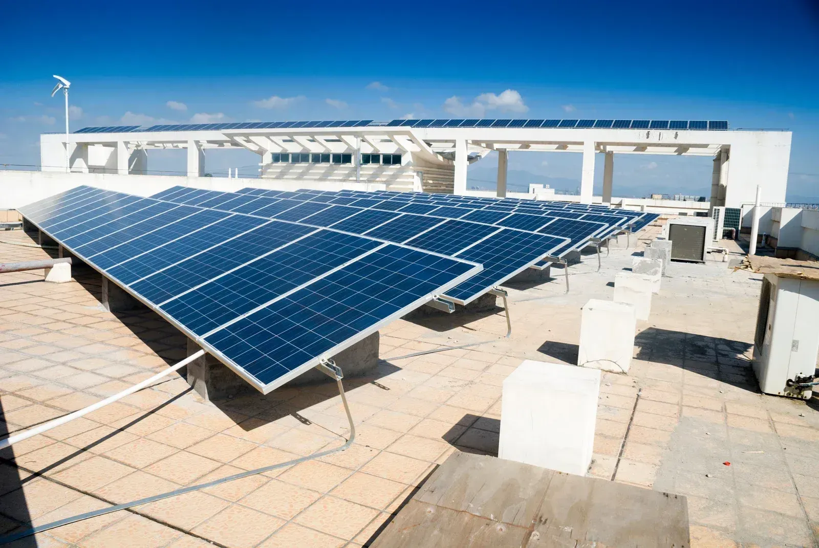 Rows of dark blue solar panels installed on a tiled flat rooftop under a clear blue sky.