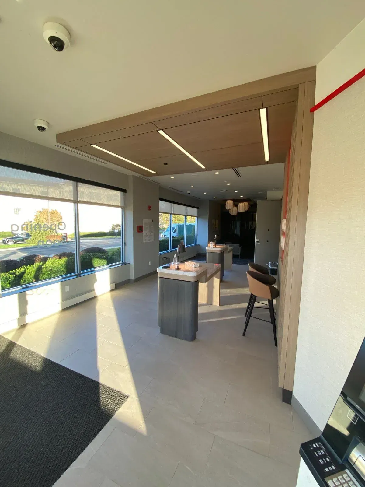 Modern bank lobby with bright natural light, minimalist counters, wood-paneled ceiling features, and seating.