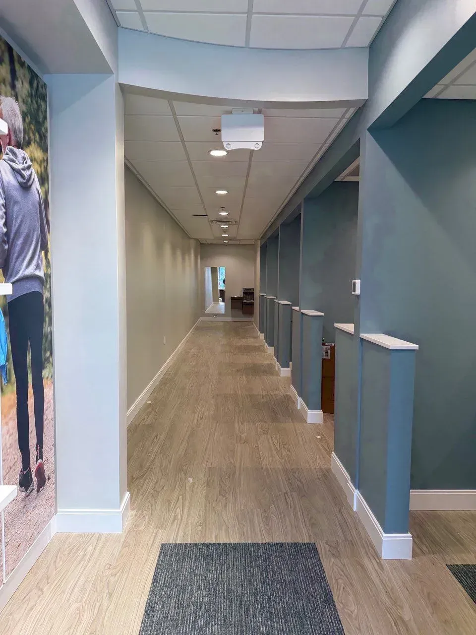 A brightly lit indoor corridor featuring a patterned rug, light wood flooring, and blue wall partitions.