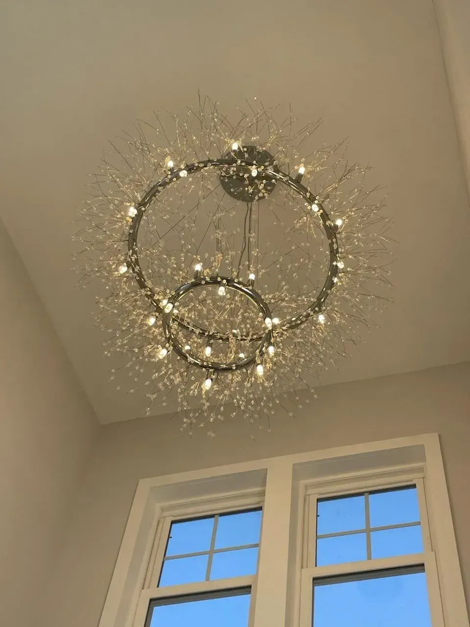 A sparkling, spherical chandelier with dual concentric rings hangs from a ceiling above a window.