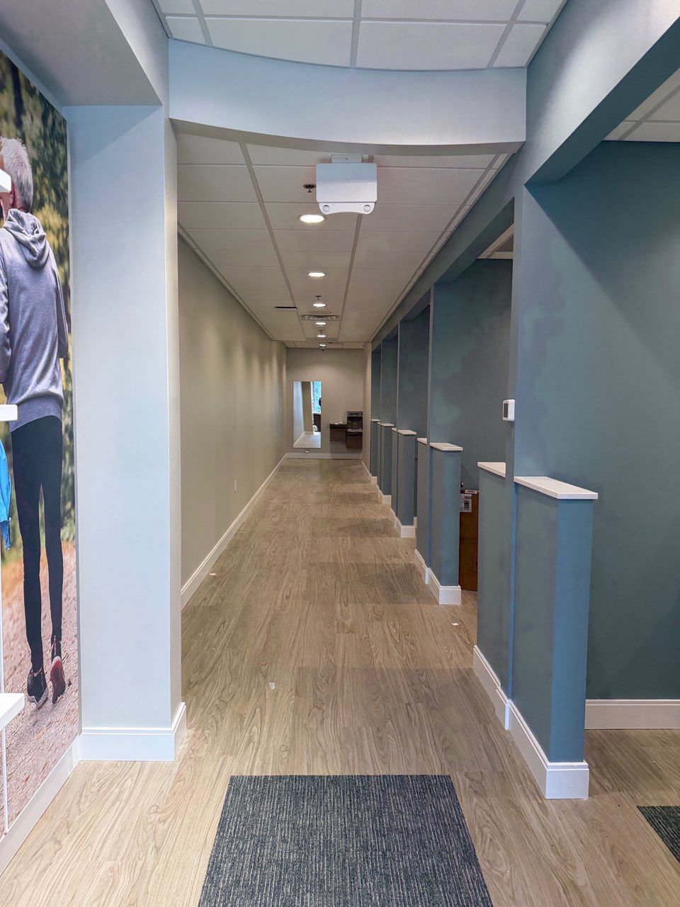 A hallway with light wood flooring, blue accent walls with partitions, and a large wall graphic of a person walking.