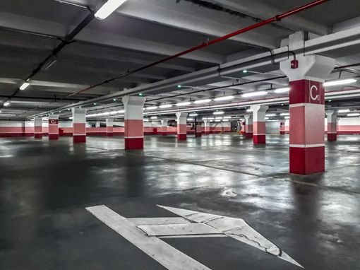 Empty parking garage with columns painted in white and red, featuring a white painted arrow on the concrete floor.