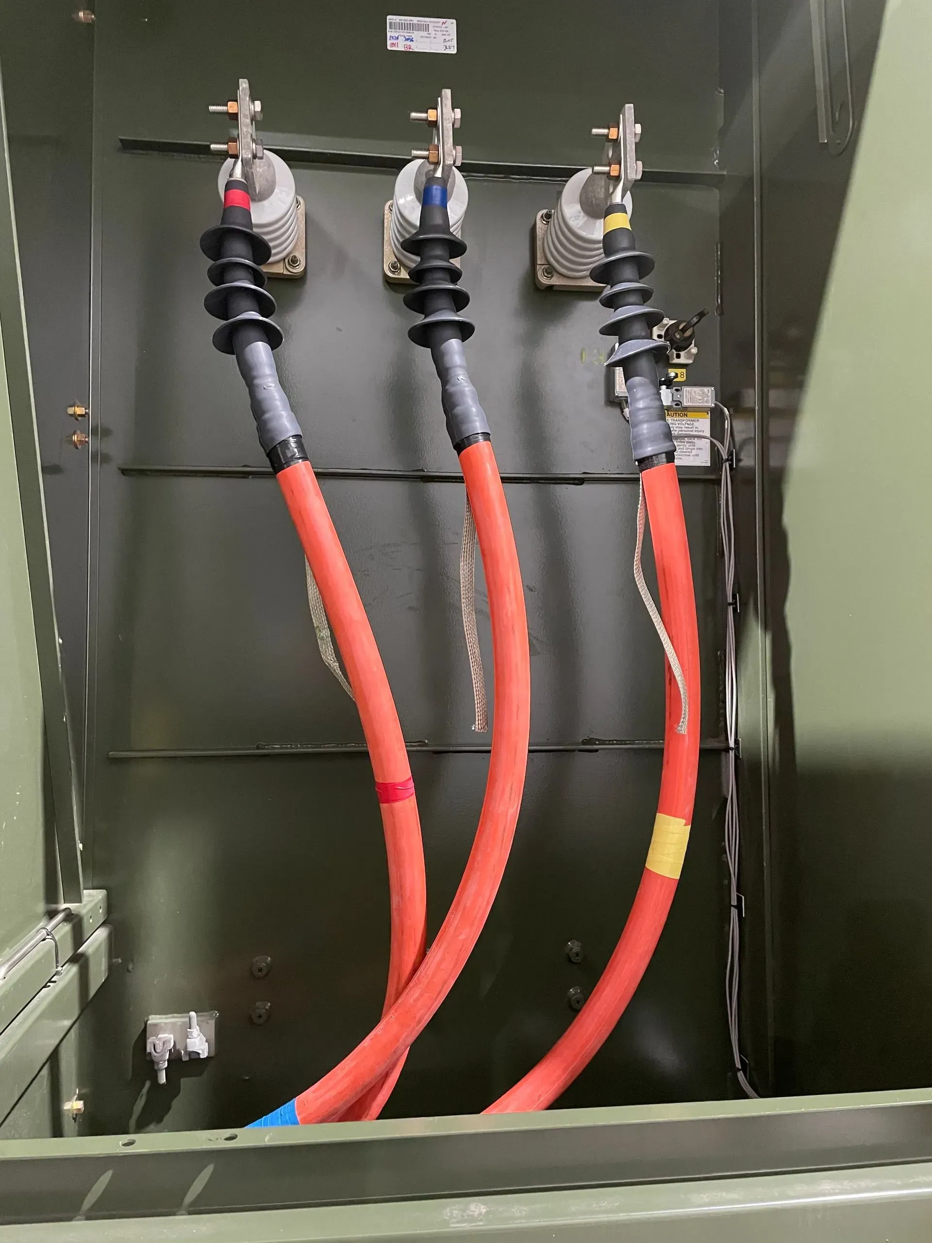 Three electrical cables with colored markings connected to porcelain insulators inside a metal equipment cabinet.