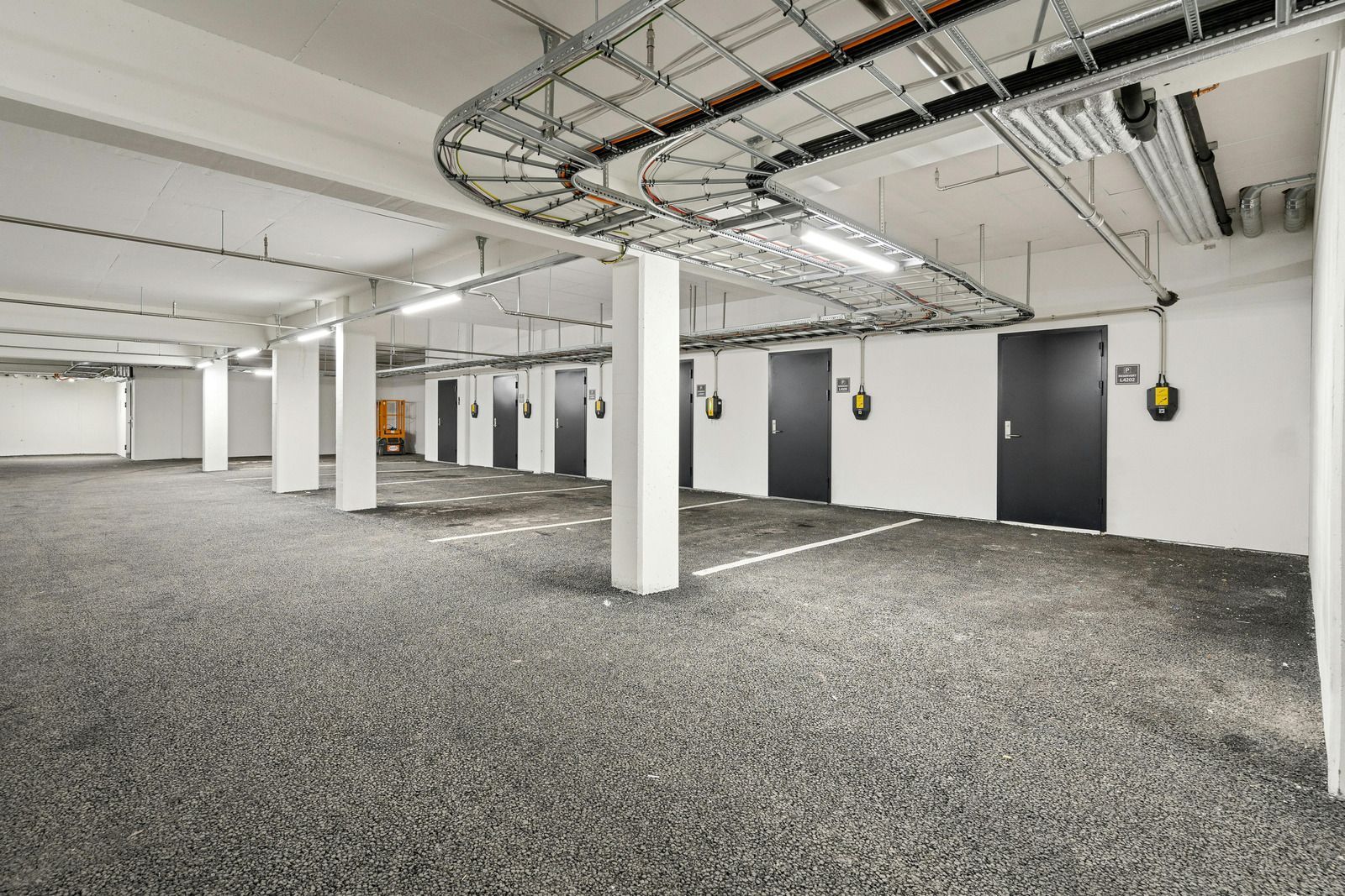 A garage interior featuring white support columns, gravel flooring, and gray storage doors lined along a white wall.