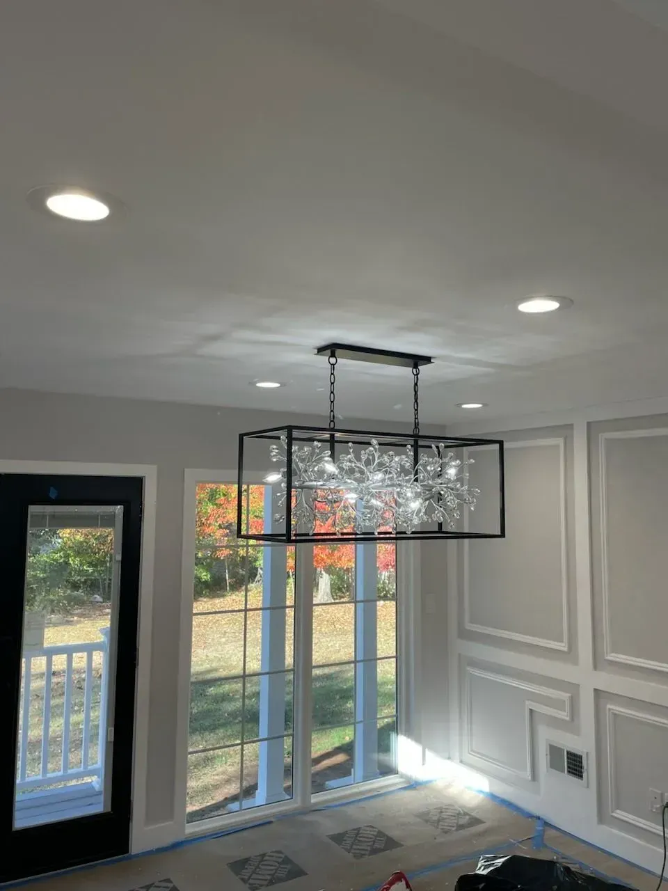 A modern black rectangular cage chandelier hangs from a ceiling above a room.