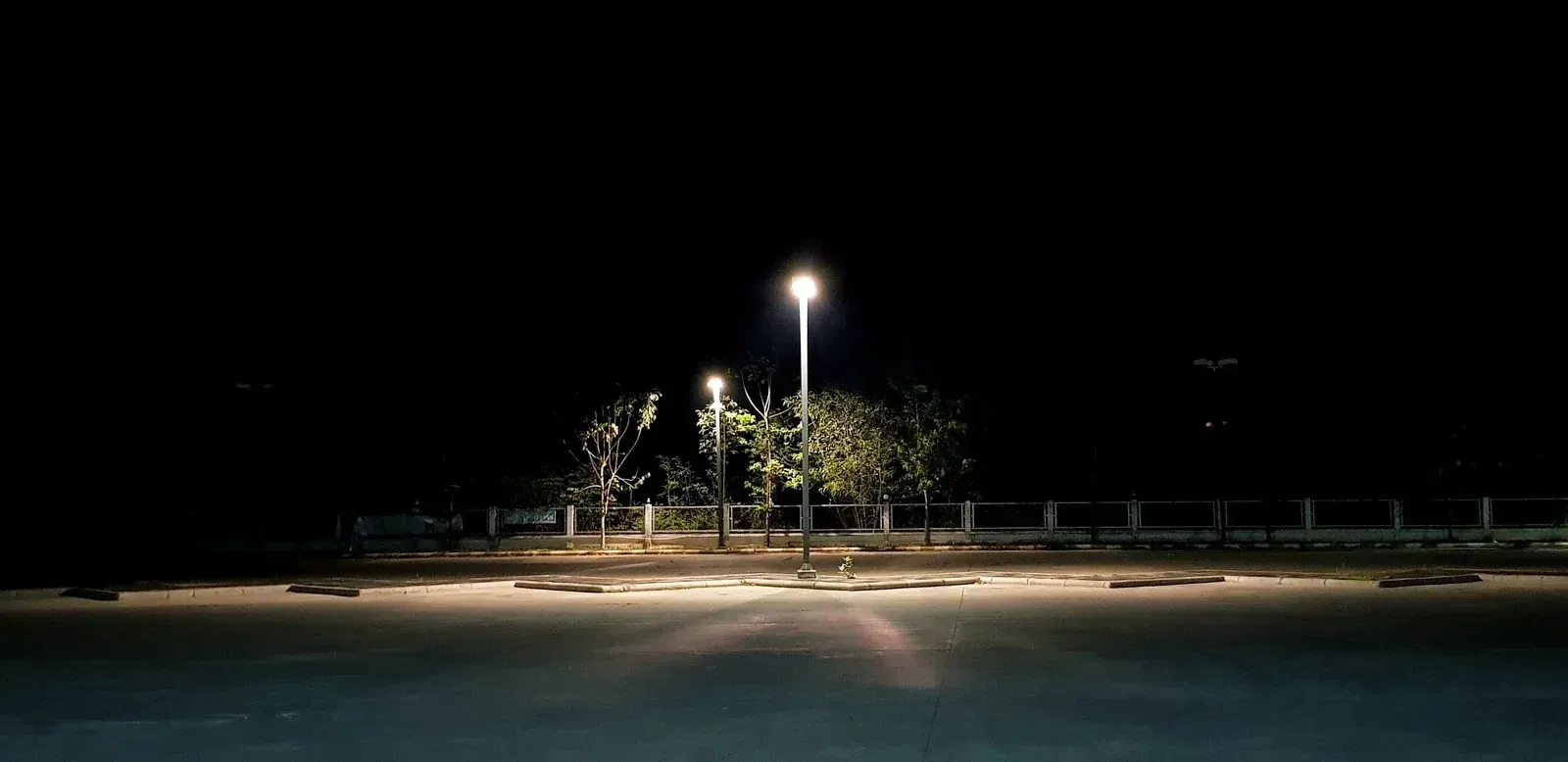 A parking lot at night illuminated by two bright streetlights casting pools of light onto the pavement.