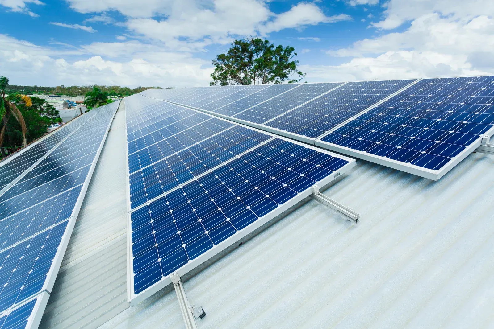 Solar panels installed on a metal roof under a blue sky with clouds.