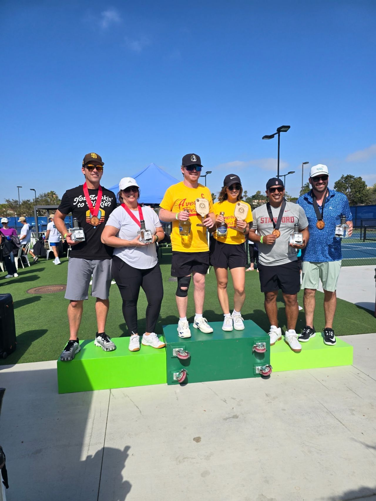 PWI 2026 Pickleball Tournament  - Three teams (six adults )with winners' ribbons stand on the podium.