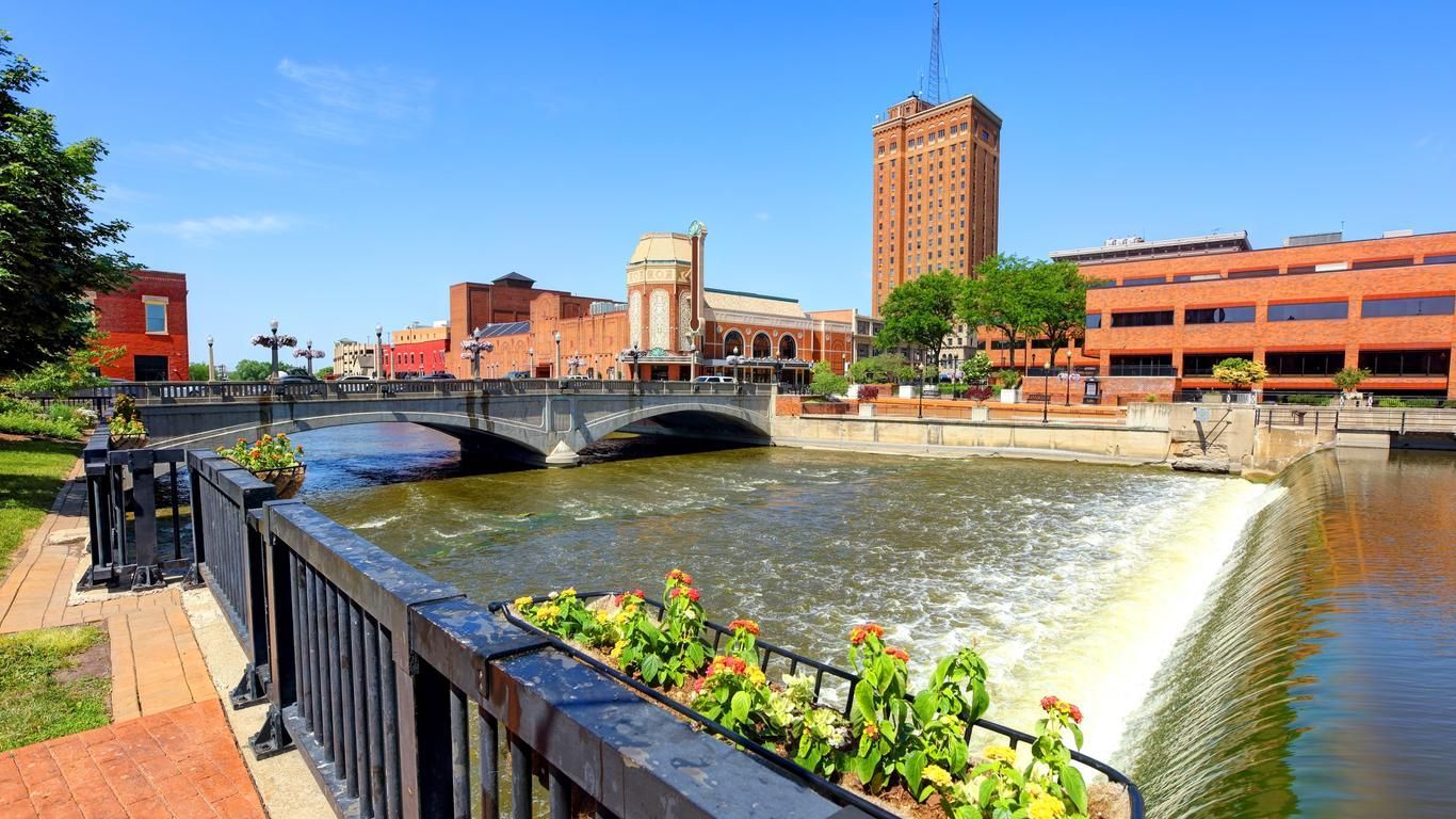 A bridge over a river in a city with a waterfall in the background. Aurora Illinois