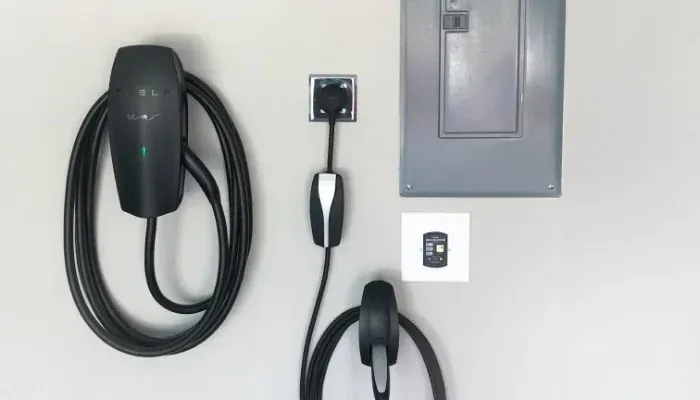 A tesla charging station is attached to a wall next to a switch.