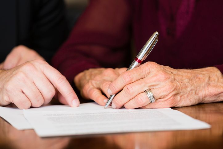 Una mujer mayor está firmando un documento con un bolígrafo.