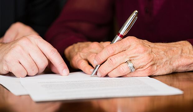 Una mujer mayor está escribiendo en un trozo de papel con un bolígrafo.