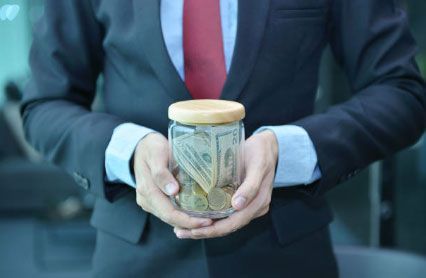 Un hombre con traje y corbata sostiene un frasco de dinero.