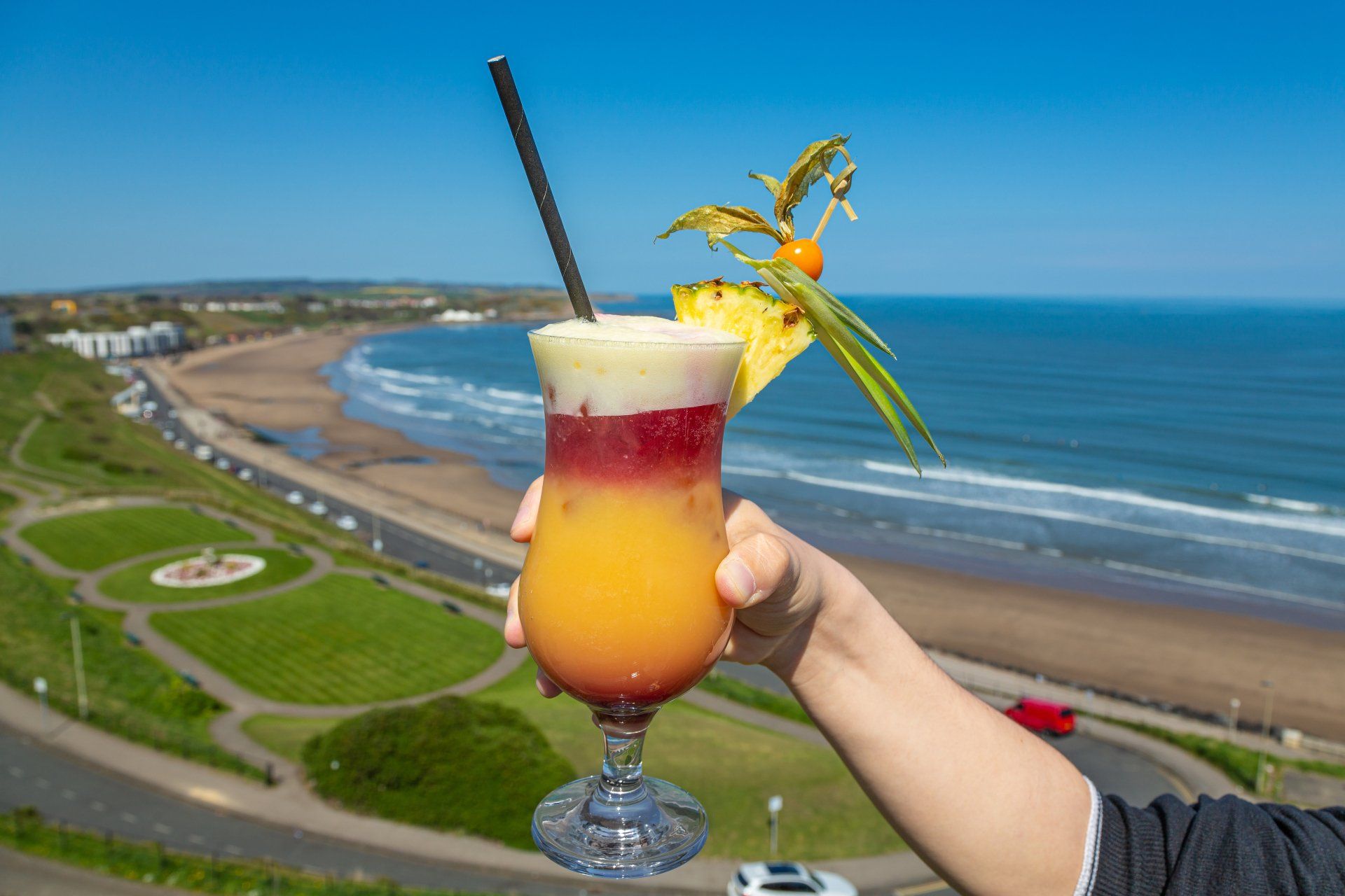 A person is holding a cocktail in front of the ocean.