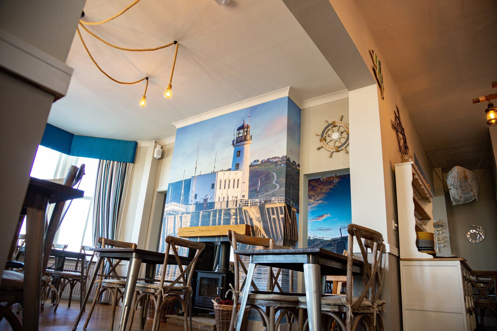 A restaurant with tables and chairs and a lighthouse on the wall.