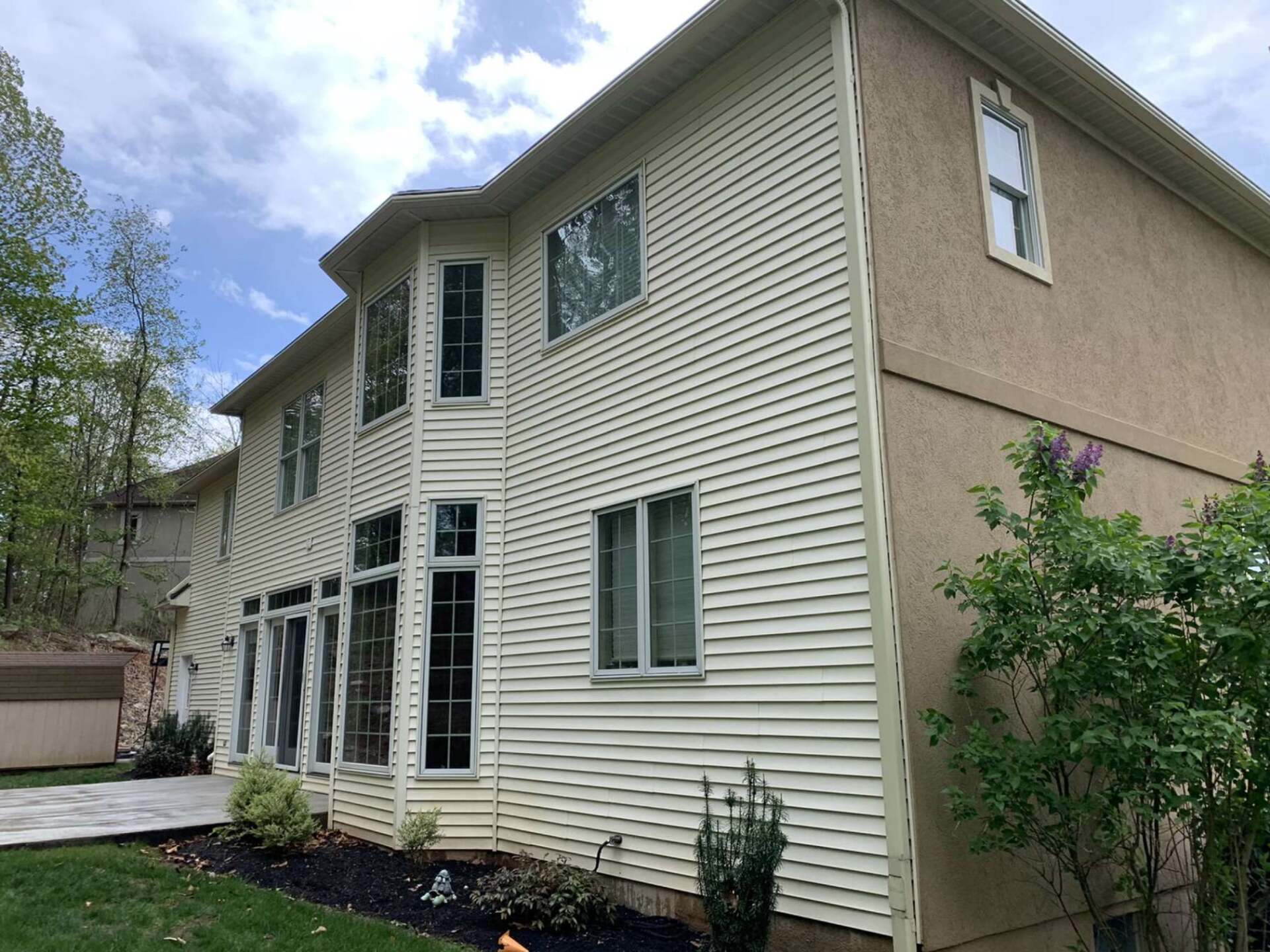Two-story house with light beige siding and windows against a cloudy sky.