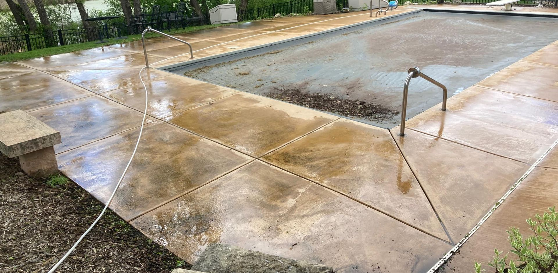Wet concrete pool deck. Pool is covered. Green plants in background.
