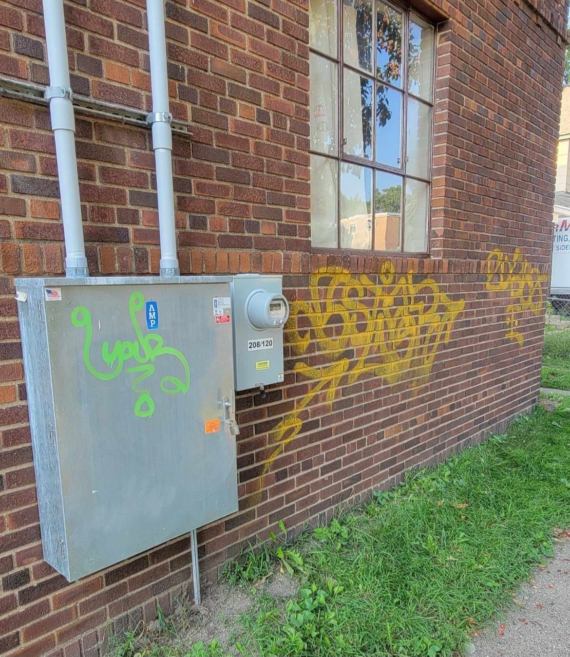Brick building exterior with electrical boxes, a window, and yellow graffiti.
