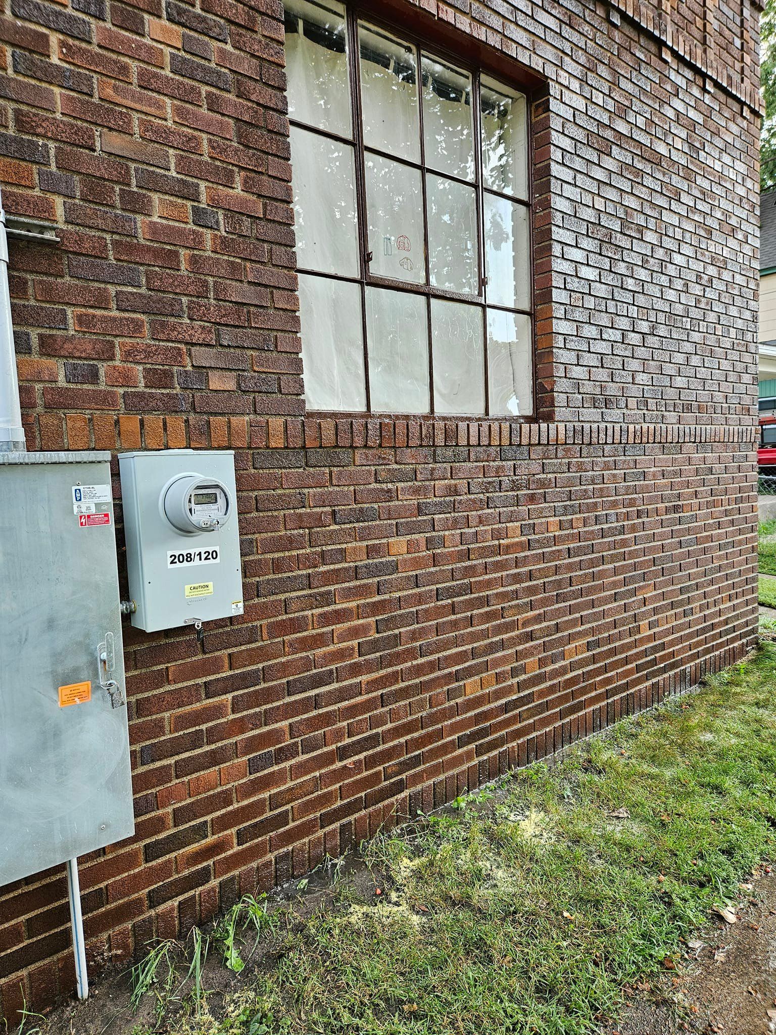 Brick building with window and electrical boxes; grass in foreground.
