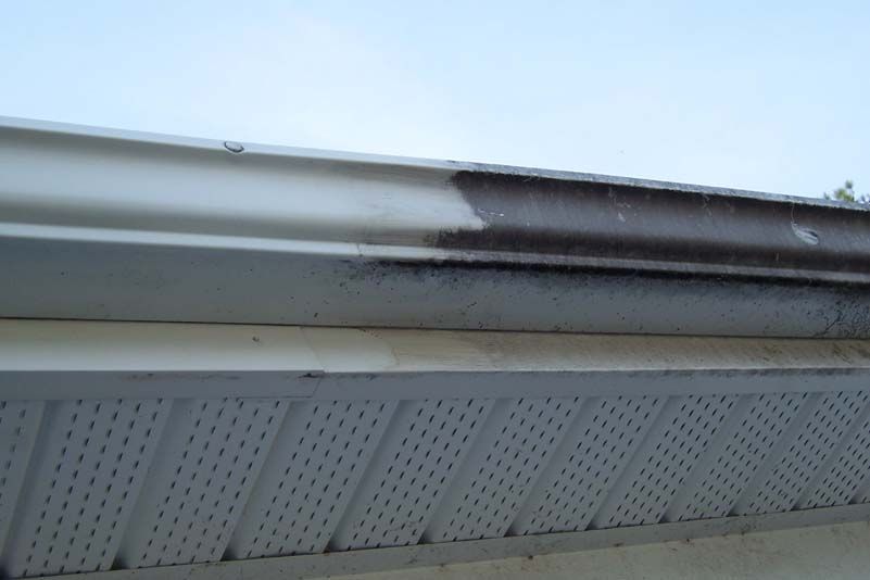 Dirty, dark streaks on white rain gutter with a beige soffit below and a light blue sky.