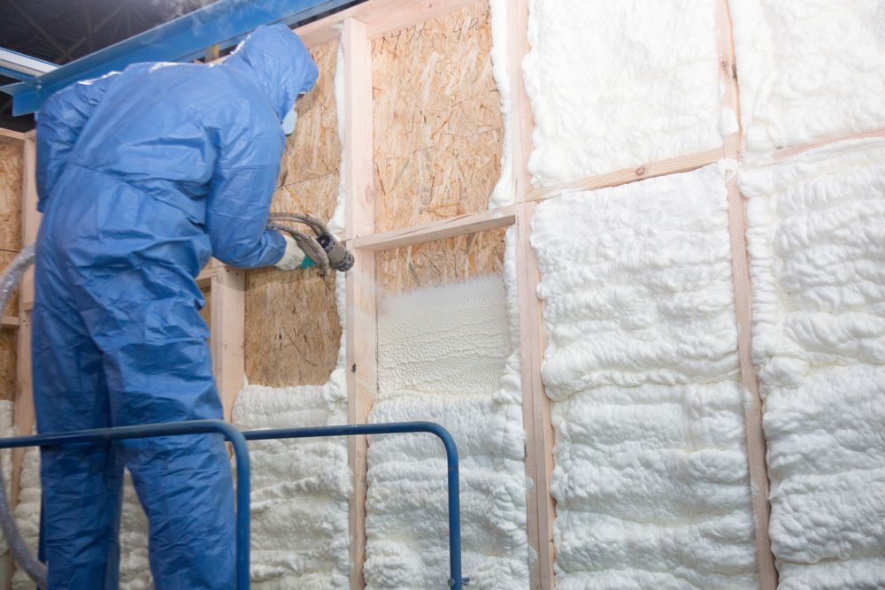 A man in a blue suit is spraying foam on a wall.