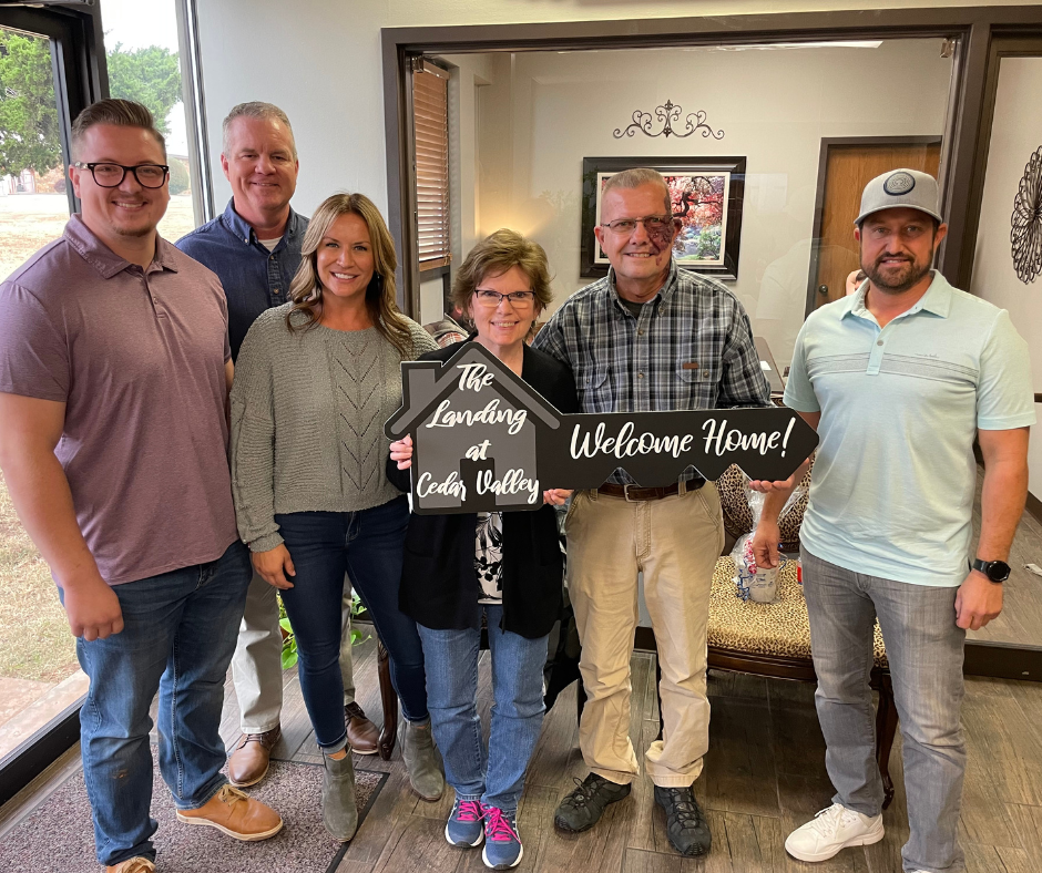 A group of people standing next to each other holding a welcome home sign.