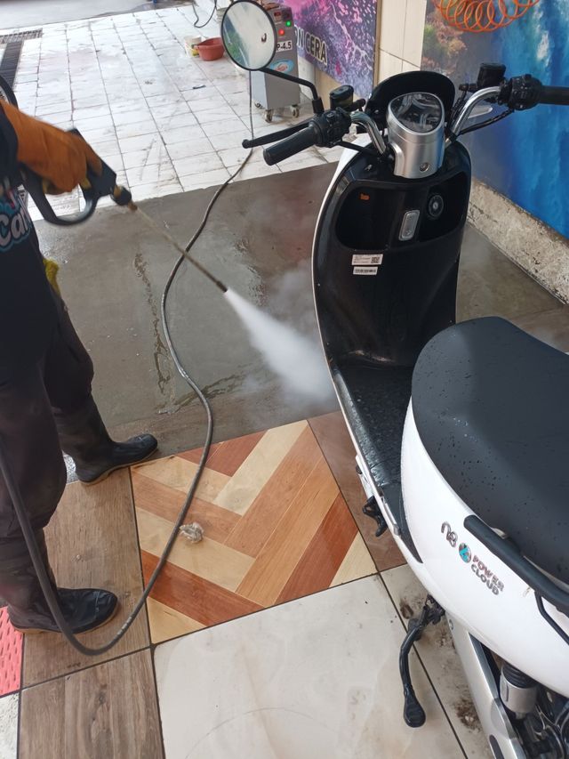 Persona limpiando con agua a presión una scooter negra en una zona exterior embaldosada