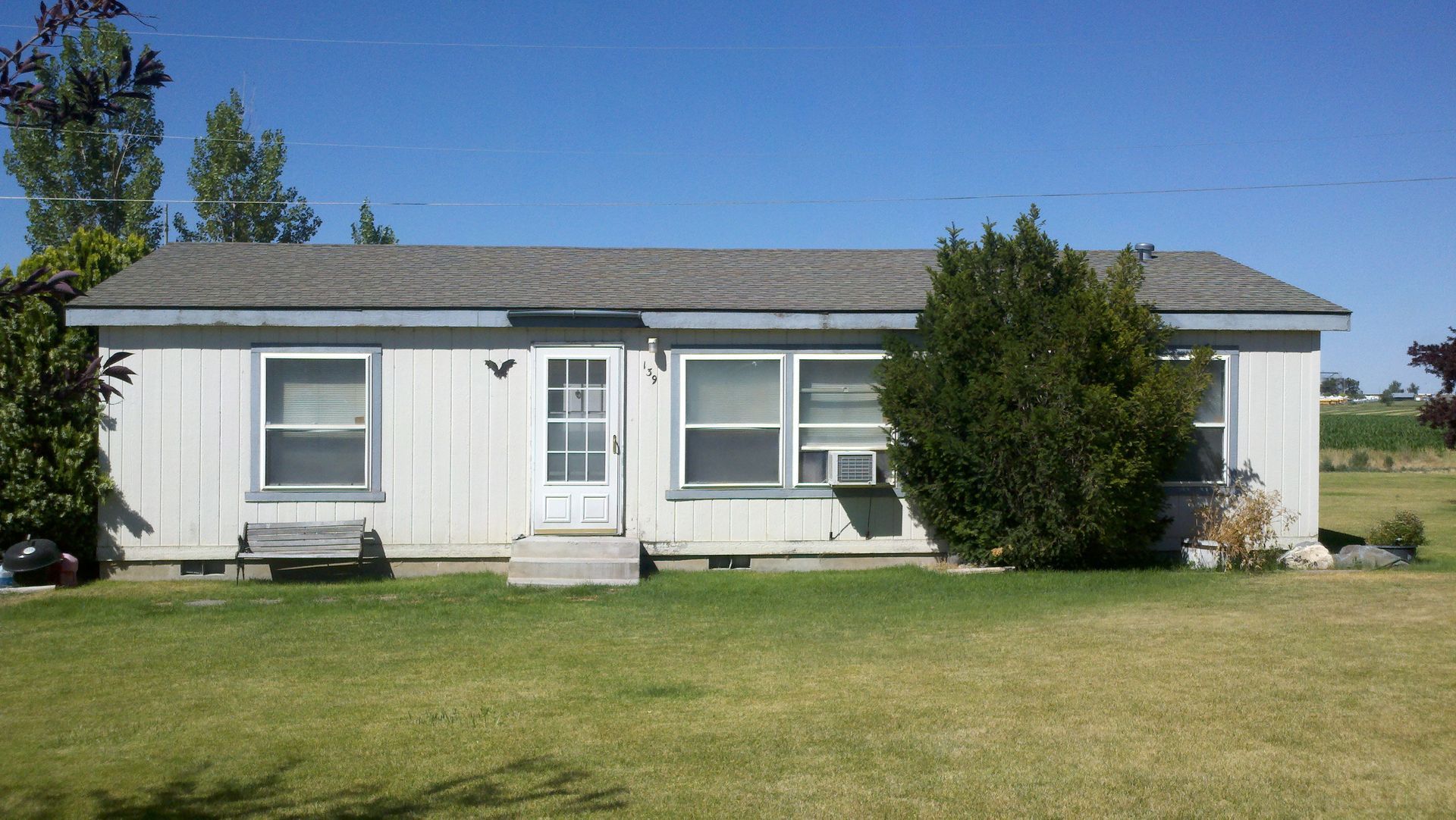 A small white house is sitting in the middle of a grassy field.